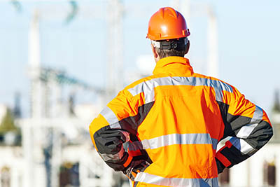 homme de dos avec blouson un haute visibilité orange et un casque de chantier