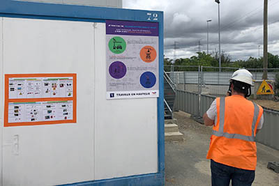 homme sur un chantier passant devant un affiche pour le permis de travaux en hauteur