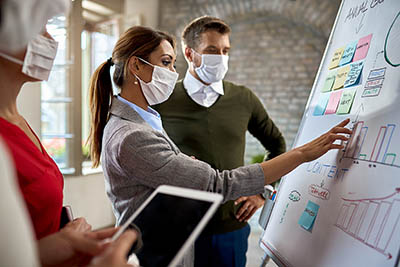 femmes et homme avec un masque de protection discutent devant un tableau blanc